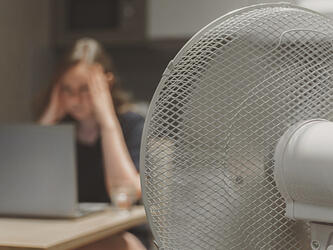 woman working at laptop in hot weather next to fan